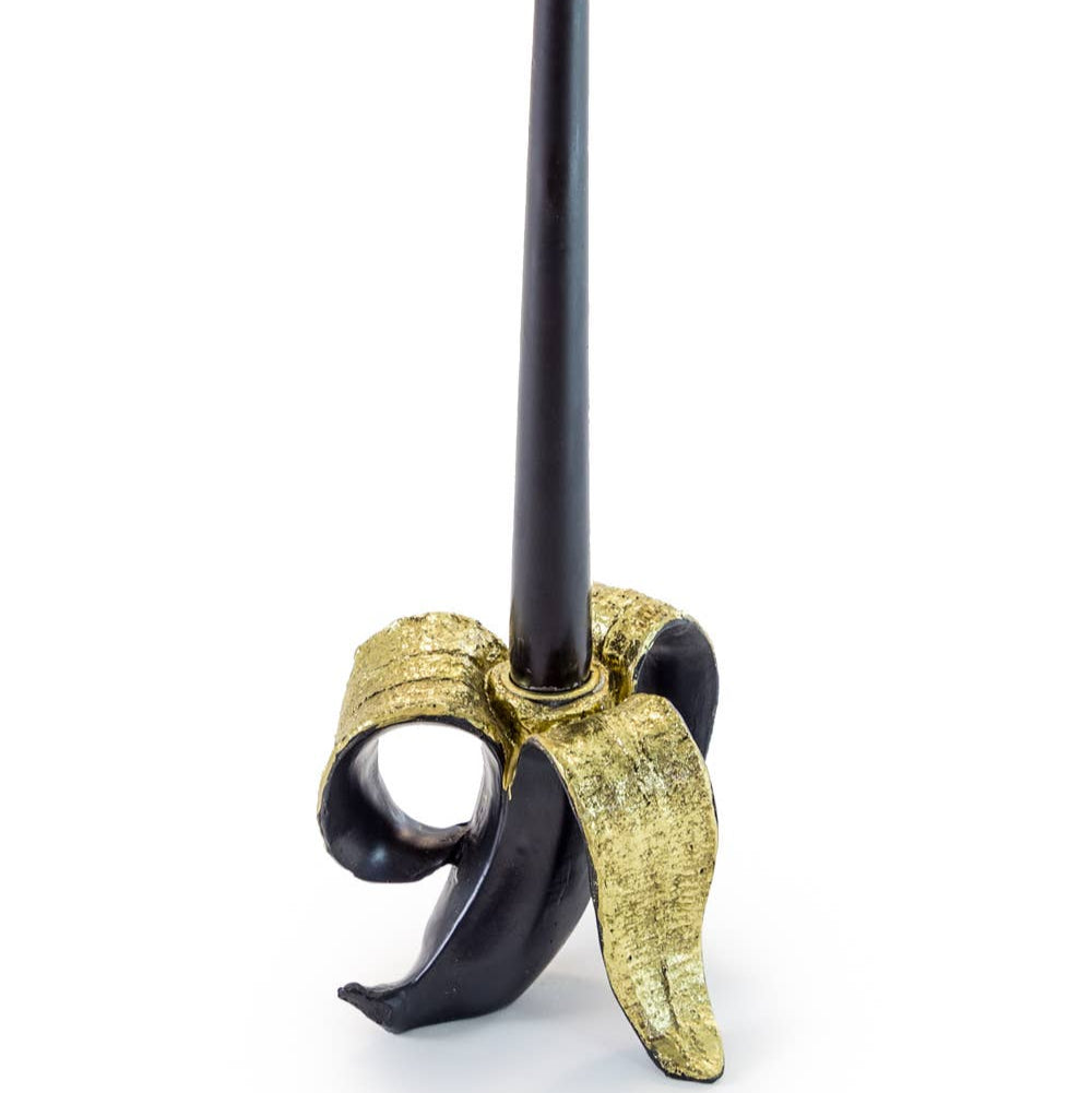 A banana-shaped candle holder with a black candle on top, featuring gold accents.