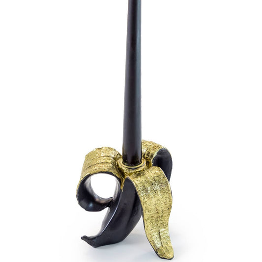 A banana-shaped candle holder with a black candle on top, featuring gold accents.