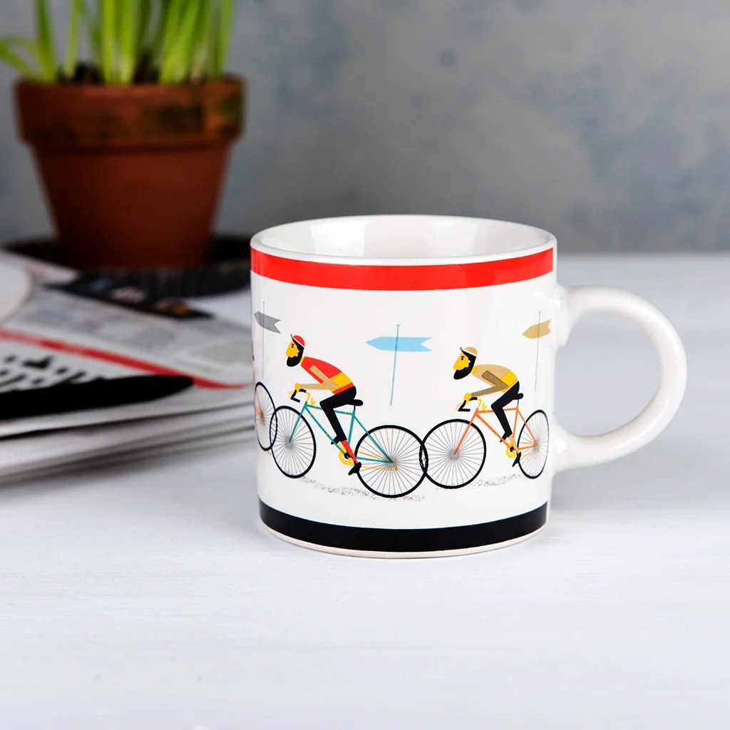 White mug with cyclist design on a table with a plant and remote control in the background
